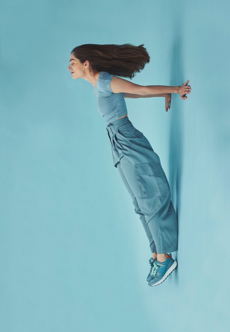 Top ajustado de color azul claro combinado con pantalones cargo sueltos de talle alto en azul. Zapatillas azules con acentos en contraste. Fondo en azul sólido.