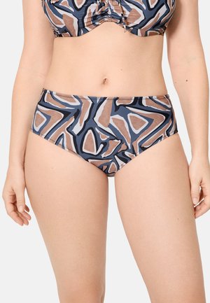Mujer con braguitas de bikini de talle alto con un patrón geométrico abstracto en colores azul, marrón, negro y blanco, de pie contra un fondo liso.