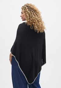 Črn pončo s trikotno obliko in dekorativnim srebrnim obrobam ob robu. Izdelan iz mehkega blaga, ki ima gladko teksturo.