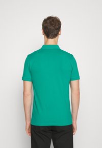 Polo vert avec un col classique et des manches courtes. Tissu en coton lisse, design simple, sans motifs ni accents visibles.