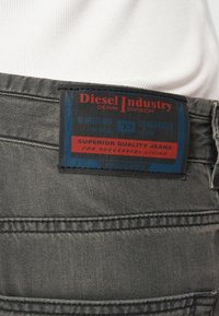 Γκρι τζιν από τζιν ύφασμα με μπλε και κόκκινη ετικέτα που αναγράφει "Diesel Industry", με κείμενο σχετικά με την ανώτερη ποιότητα και την εγγραφή από το 1978.