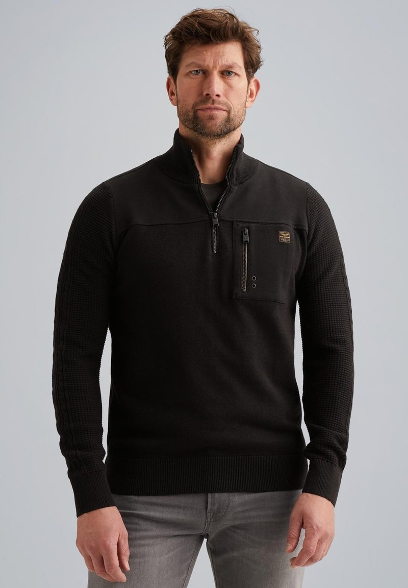 Schwarzer Zip-Pullover mit gestrickten Texturärmeln und einer Brusttasche. Verfügt über einen hohen Kragen und gerippte Bündchen, hergestellt aus einem weichen Stoffgemisch.