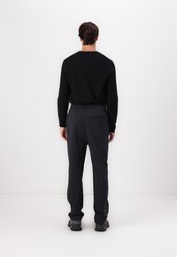 Black sweater, gray elastic-waist pants with a rear pocket, smooth texture, and logo detail on the left leg. Casual, sporty style.