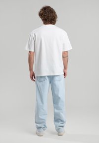 White short-sleeve t-shirt with a relaxed fit, paired with light blue loose-fitting jeans and white sneakers. Simple, casual design.