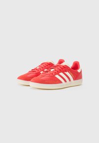Røde sneakers med hvidt tre-stribet design og cremede accenter. Lavet af stof og ruskind. Rund tå og tekstureret gummisål.