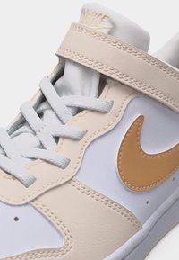 Λευκό και μπεζ αθλητικό παπούτσι Nike με λογότυπο Swoosh σε αποχρώσεις καφέ, λευκά κορδόνια και μπεζ λουράκι πάνω από τη γλώσσα.