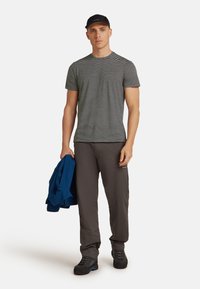 Pruhované černobílé tričko, šedé kalhoty a černé boty. Drží modrou bundu. Neformální design, krátké rukávy a jednoduchý vzor.