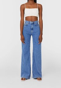 Witte cropped top met dunne bandjes, gecombineerd met high-waisted blauwe wijde jeans. Gladde denims textuur, lichte wassing kleur en een ontspannen pasvorm.