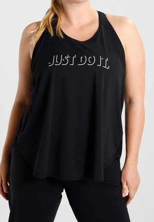 Kvinde iført en sort, ærmeløs atletisk top med hvid tekst "JUST DO IT" og sorte bukser, stående mod en ensfarvet baggrund.