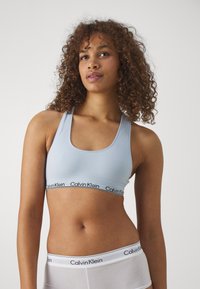 Svetlomodrá športová podprsenka so širokým čiernym pásom s logom Calvin Klein, s okrúhlym výstrihom a dizajnom s pretekárskym chrbtom, vyrobená z hladkej látky.