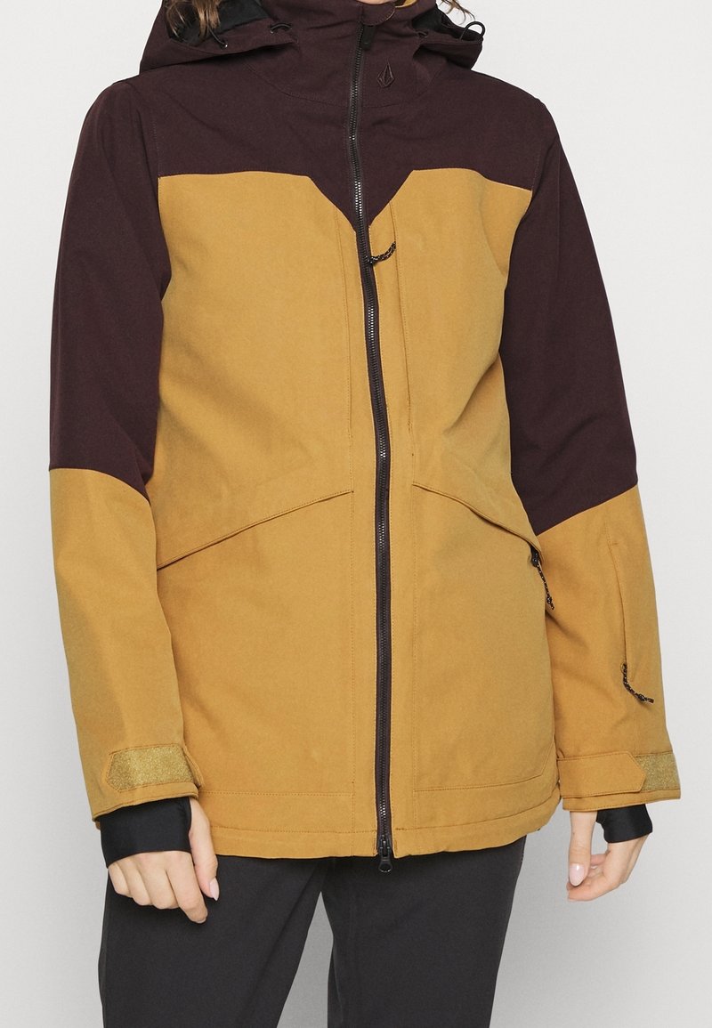 Wasserabweisende Jacke mit Reißverschluss vorne. Verfügt über ein Design mit braunem und senfgelbem Farbschema, eine verstellbare Kapuze und Klettverschlussmanschetten.