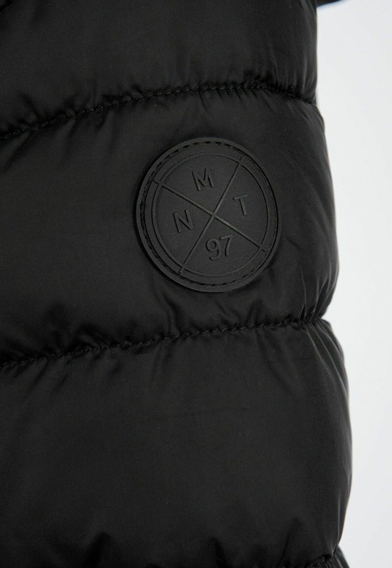 Sezione di giacca a vento nera imbottita con pannelli cuciti e una toppa in gomma testurizzata con motivi a croce e le lettere "MNT" e "97."