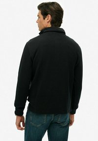 Czarny polarowy sweter z wysokim kołnierzem, długimi rękawami i luźnym krojem. Posiada ściągacze przy mankietach oraz gładką fakturę.
