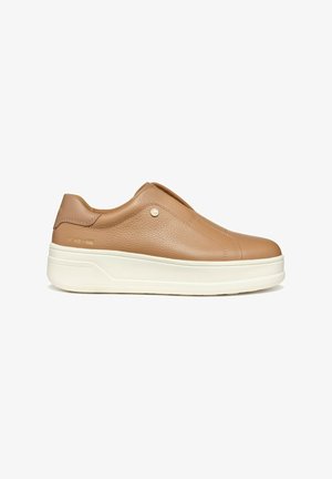 Scarpa slip-on in pelle marrone chiaro con un design minimalista, suola bianca, cuciture sottili e un piccolo accento metallico sul lato.