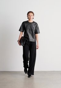 Top preto de couro de mangas curtas com decote redondo, combinado com calças largas pretas e uma clutch oversized combinada. Design minimalista.