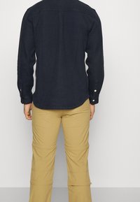 Mörkblå, långärmad skjorta med texturerad väv, knappade manschetter och svängd fåll. Bärs tillsammans med beiga, zippered byxor med avslappnad passform.