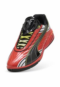 Scarpa sportiva rossa e nera con finitura lucida, dotata di lacci gialli, superficie testurizzata, fori di ventilazione e distintivi accenti bianchi.