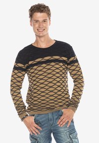 Schwarzer und brauner gestrickter Pullover mit einem strukturierten Diamantdesign, rundem Ausschnitt und langen Ärmeln, kombiniert mit blauen Cargo-Hosen.