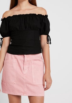 Top nero scollato con scollo arricciato e corpetto aderente; abbinato a una gonna di jeans rosa con tasche frontali e chiusura a bottone.