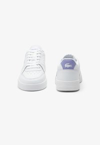 Białe skórzane sneakersy o gładkiej fakturze, fioletowe akcenty na pięcie oraz perforowane detale po bokach. Klasyczny design z sznurowaniem.