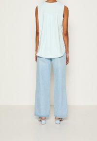 Haut sans manches bleu clair avec un ourlet arrondi, associé à un jean large en denim clair et des sandales à talons bleu clair. Design simple, texture lisse.