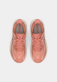 Baskets de sport légères en corail clair avec tige en maille et accents texturés. Présentent des lacets plats, une semelle rembourrée et un logo HOKA sur la languette.