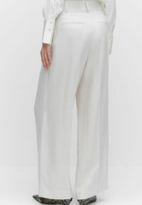 Witte, wijde broek met een gladde textuur, voorzien van twee achterzakken en een getailleerde tailleband, gecombineerd met patroonschoenen.