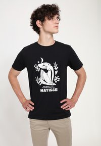 Camiseta de algodón negra con un gráfico blanco de una figura reclinada, estrellas y plantas, con el texto "MATISSE" en la parte inferior.