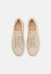 Beige Leder-Sneaker mit weißen Gummisohlen, runder Zehenform, Schnürdesign und einem dezenten gelben Akzent an der Ferse.