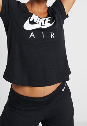 Persona con camiseta negra Nike Air y leggings negros Nike, brazos levantados, recortada a la altura del pecho y las caderas sobre un fondo liso.
