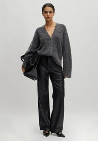 Grijze wollen cardigan met een diepe V-hals en knoopsluiting, gecombineerd met hoogwaardige zwarte kunstlederen broeken en een zwarte tas.