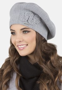 Beret gri tricotat, cu trei accente florale și detalii din perlă, având o textură moale și un design lejer.