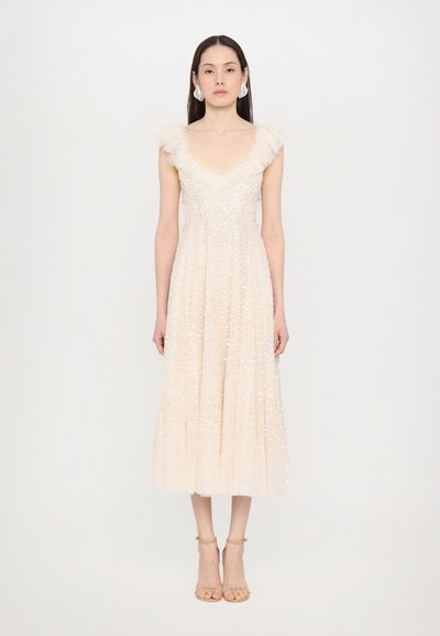 Une robe sans manches de couleur beige clair avec un décolleté en V, des détails de volants aux épaules, et ornée de sequins sur tout le tissu.