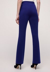 Koboltblå utsvängda byxor med en slät yta och ett åtsittande midjeband, tillsammans med svarta högklackade skor. Bakifrån visar de rena linjer.