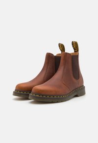 Braune Chelsea-Boots aus Leder mit elastischen Seitenpaneelen, runder Spitze und gelben Nähten, ausgestattet mit Anziehschlaufen für einen einfachen Einstieg.