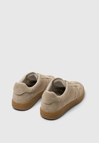 Beżowe zamszowe sneakersy o teksturowanej powierzchni, okrągłym nosku i gumowej podeszwie. Charakteryzują się brązowymi akcentami na podeszwie oraz niskim krojem.