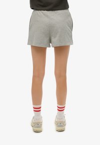 Pantalones cortos de algodón gris con un ajuste relajado, combinados con calcetines blancos con rayas rojas y zapatillas beige. Detalle visible de la cinturilla elástica.