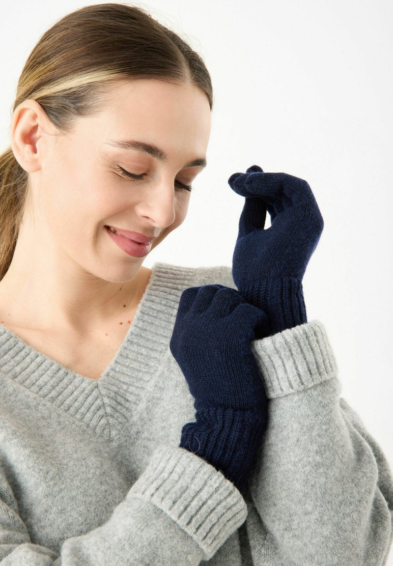Marineblaue Strickhandschuhe mit gerippten Bündchen werden an den Händen getragen, kombiniert mit einem hellgrauen V-Ausschnitt-Pullover mit strukturiertem Muster.