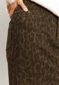 Pantalons en denim kaki avec un motif léopard foncé, dotés de poches latérales et d'accents en métal argenté. Tissu épais avec une finition texturée.