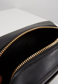 Musta nahkainen pussukka kultaisella vetoketjulla. Sisäpuoli on vuorattu mustalla kankaalla ja sisältää pienen taskun. Pussukan pinta on sileä ja muoto suorakaiteen muotoinen.