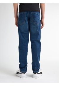 Tmavě modré džíny s volnějším střihem, se dvěma zadními kapsami s prohnutým švem, doplněné bílými teniskami.