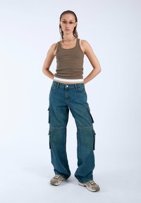 Jeans cargo en denim de lavado medio, con bolsillos laterales, un ajuste holgado y una pierna ligeramente acampanada. Combinados con una camiseta sin mangas ajustada color marrón.
