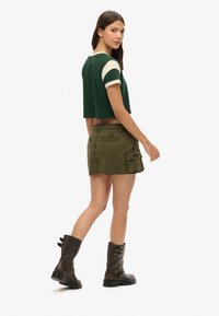 Groene cropped t-shirt met roomkleurige mouwen, olijfgroene cargoshorts met zakken en zwarte legerlaarzen. Eenvoudig ontwerp met functionele elementen.
