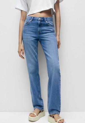 Jeans azzurri a vita alta con gamba dritta, design classico a cinque tasche e un leggero sbiadimento. Indossati con un top bianco corto e sandali.