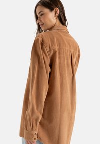 Bruine corduroy shirt met lange mouwen, knoopmanchetten en een rugpand. Kenmerkt zich door een verticale ribbelstructuur en een ontspannen pasvorm.