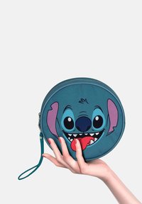 Ronde teal tas met een afbeelding van het gezicht van een cartoonfiguur, met grote ogen, een open mond en een opvallende tong. Bevat een polsbandje.