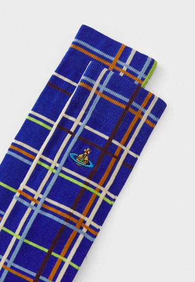 Blå rutete sokker med et rutenettmønster i hvite, oransje, grønne og blå linjer. Brodert logo av en karakter på en båt.