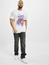 Hvit t-skjorte med et fargerikt grafisk trykk av en basketballspiller. Kombinert med mørke jeans og hvite joggesko. Enkelt, uformelt design.