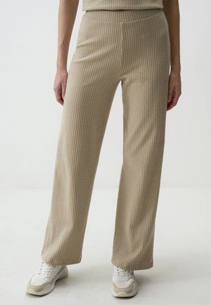 Beige ribbed knit pants with a high waist, wide legs, and a textured finish, paired with white and beige athletic shoes.
