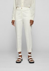 Białe, dopasowane spodnie o prostym kroju, z podwiniętymi mankietami i gładką fakturą, zestawione z masywnymi białymi sandałami.